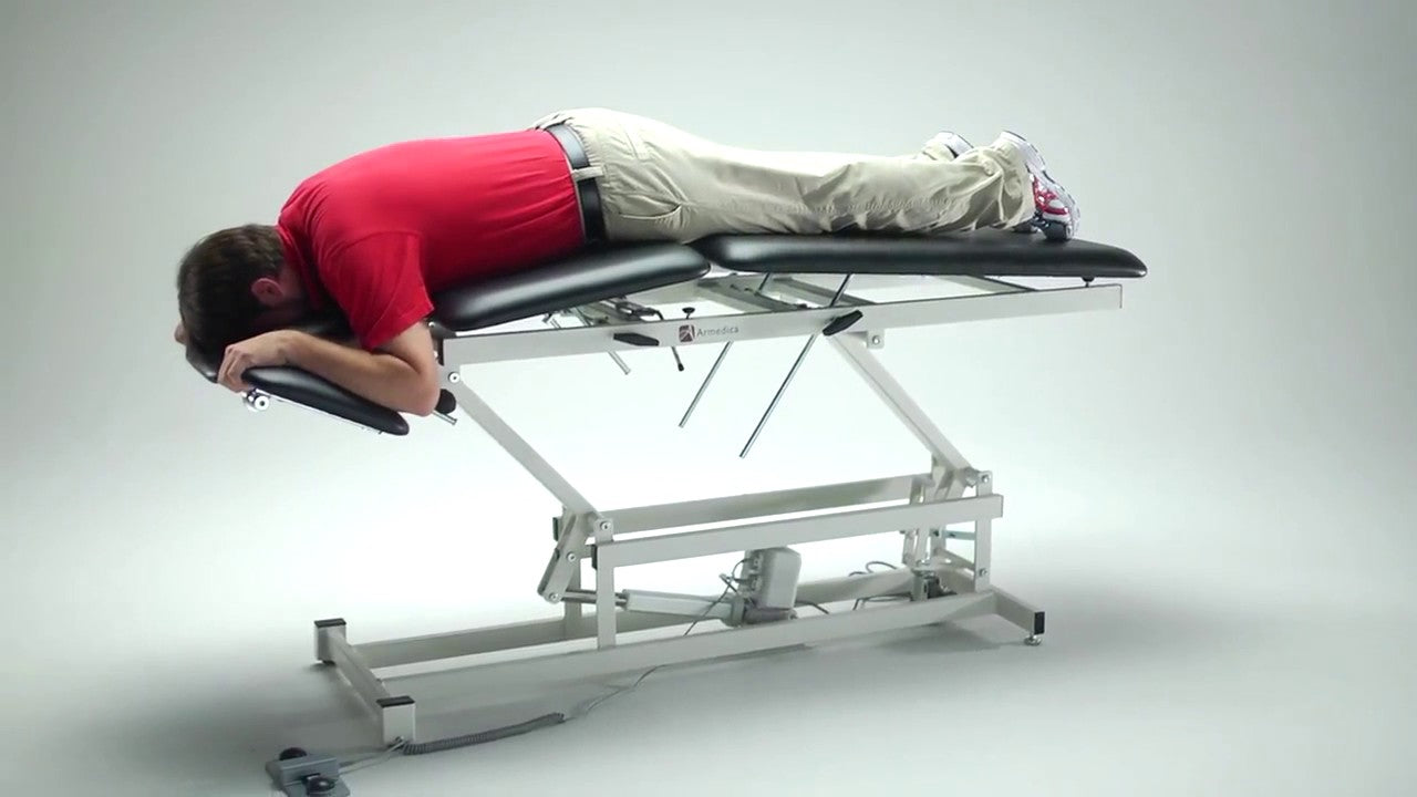 Person lying on a hydraulic lift table against a gray background